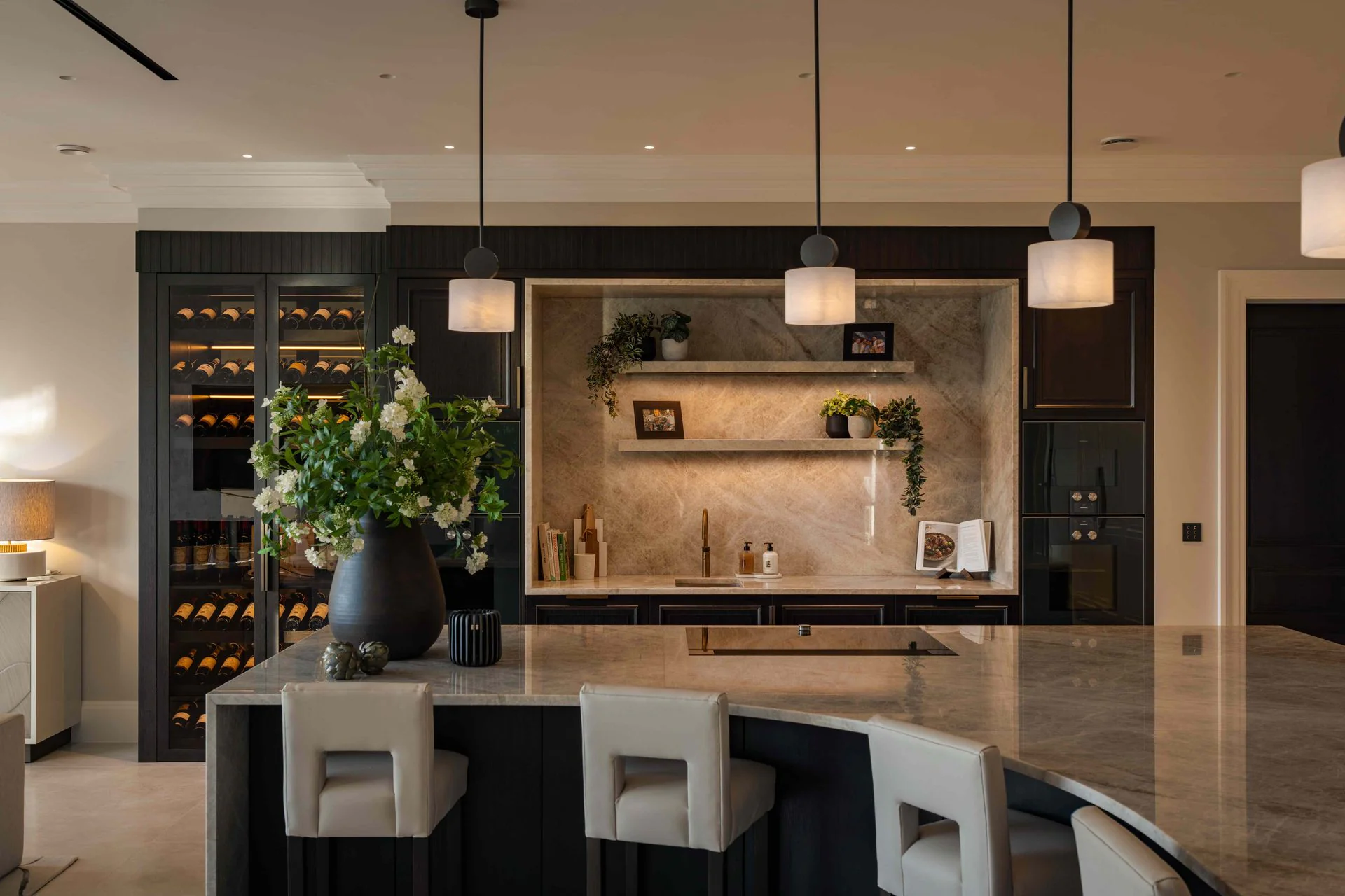 Dark kitchen with a marble island, three pendant lights and a wine cabinet
